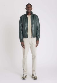 Groene leren bomberjack met geribde manchetten, een ritssluiting en een crèmekleurige trui. Gecombineerd met lichtgrijze broek en beige sneakers.