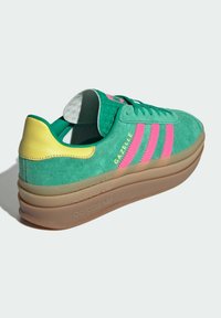 Gröna mockasneakers med gula häldetaljer, rosa tre ränder och upphöjd gummisula. Har en vadderad tunga och texturerad innersula.