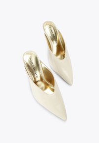 Beige lakleren muiltjes met een spitse neus en een open achterkant. Het interieur heeft een metallic gouden binnenzool en het merkembleem gedrukt.