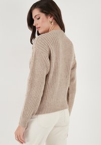 Beige knitted sweater with a textured pattern, ribbed cuffs and hem, featuring a round neckline and slightly relaxed fit.