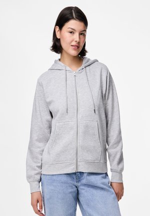 Sudadera con cremallera gris hecha de una tela suave y texturizada, con bolsillos frontales y capucha con cordón. Llevada sobre unos jeans de mezclilla azul claro.