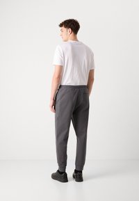 Pantaloni de jogging gri cu un talie elastică, design tapered, buzunare laterale și mansete ribbed. Purtați cu un tricou alb simplu și adidași negri.
