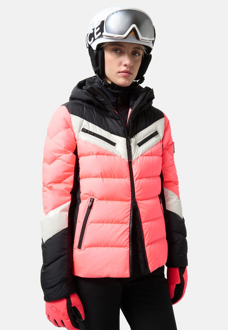 Pink and black insulated ski jacket with a hood, featuring zippered pockets and chevron patterns in black and white. Gloved hands are visible.