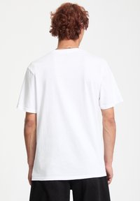 Hvid bomulds t-shirt med rund hals og korte ærmer, der har et ensfarvet design og en afslappet pasform. Båret med sorte bukser.