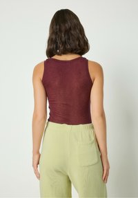 Burgundy figurnära linne med rund halsringning, tillsammans med ljusgröna vida byxor som har en bakficka och texturerad tyg.