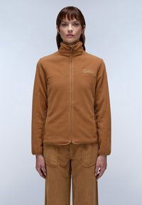 Braune Fleecejacke mit hohem Kragen und Frontreißverschluss; verfügt über ein dezentes Logo auf der Brust und strukturierter Stoff; kombiniert mit passenden Cordhosen.