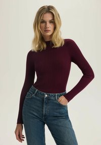 Burgundowa, ribbedowa bluzka z długim rękawem i wysokim kołnierzem, w połączeniu z niebieskimi dżinsami z wysokim stanem i pięcioma kieszeniami.