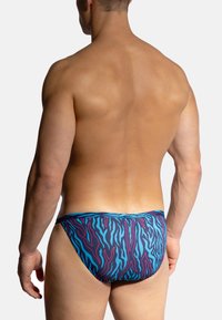 Herren-Schwimmbreve mit einem blauen und lila Tigerstreifenmuster. Das Material wirkt glatt und dehnbar, mit einem enganliegenden Design ohne zusätzliche Verschlüsse.