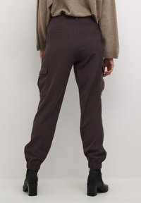 Pantalons cargo violets avec poignets élastiques, dotés de deux poches latérales, d'une texture lisse et d'une taille haute. Portés avec des bottines noires.