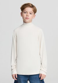 Koszulka z długim rękawem i golfem w kolorze ecru, wykonana z miękkiej tkaniny. Posiada dopasowany kołnierz i prosty krój, zestawiona z dżinsowymi szortami.