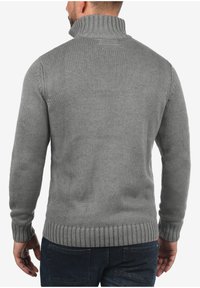 Grijze gebreide trui met een hoge geribbelde kraag, lange mouwen en geribbelde tailleband, met een textuurpatroon op de stof.