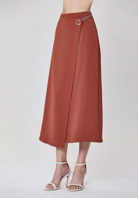Jupe midi couleur rouille avec taille haute, design enroulé à l'avant, accent en chaîne argentée à la taille, et texture de tissu lisse et fluide.