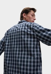 Camisa de cuadros en azul marino y blanco, con cuello clásico, mangas largas y un corte relajado. El material parece suave con una textura lisa.