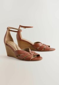 Sandalias de cuña de cuero marrón con la punta abierta, diseño de tiras entrelazadas, correa para el tobillo y un tacón de madera texturizada.