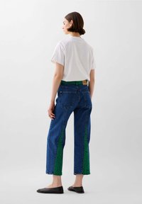 Jeans di denim con pannelli laterali verde a motivo, lavaggio blu, taglio dritto, abbinati a una maglietta bianca semplice e ballerine nere.