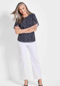 Marineblauwe blouse met stippen, voorzien van een keyhole-halslijn en korte vlindermouwen, gecombineerd met witte wijde broekspijpen en zwarte hakken.