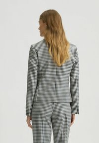 Kostkovaná sako v námořnické a bílé gingham vzoru, slim fit, se striktními ramenními vycpávkami a odpovídajícími kalhotami, látka vypadá hladce a texturovaně.