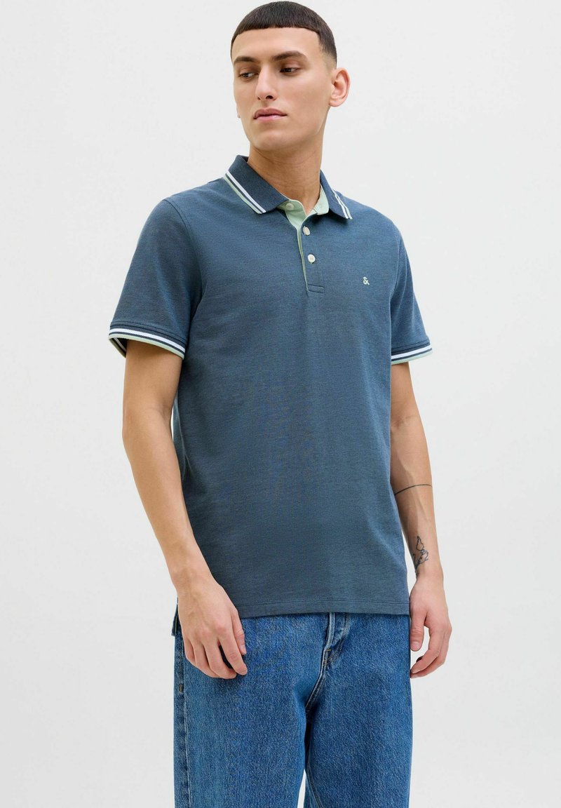 Donkerblauwe poloshirt met contrasterende lichtgroene kraag, korte gestreepte mouwen en een knoopsluiting met drie knopen. Slim fit met subtiele textuur.