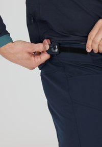 Dunkelblaue Hose aus strukturiertem Material. Der Bund verfügt über einen Klettverschluss und eine Reißverschlusstasche an der Seite.