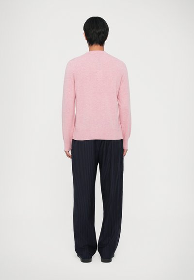Fényes rózsaszín kötött pulóver hosszú ujjal, kerek nyakkivágással és slim fit stílusban, sötétkék csíkos nadrággal párosítva, hátulról nézve.