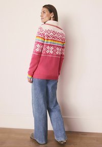 Gebreide trui met een roze lichaam, witte sneeuwvlokpatronen en meerkleurige strepen bij de halslijn. Gekocht bij een brede denim jeans in blauw.