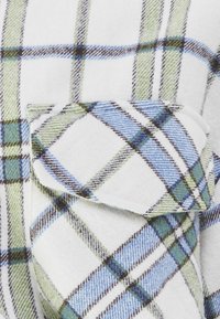 Camicia in flanella con base bianca e motivo a quadri verde, blu e nero. Include una tasca a toppa sul lato sinistro.