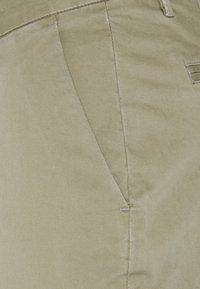 Detailní záběr na béžovou khaki látku s viditelným šitím a švem kapsy.