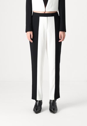 Black and white tailored trousers featuring a vertical color block design, smooth fabric, and a tapered fit, paired with black heeled boots.