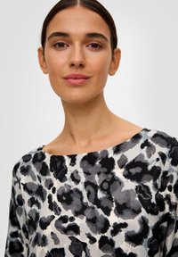 Top à imprimé léopard dans des tons de noir, gris et crème ; fabriqué en tissu texturé avec un large col et des manches courtes.