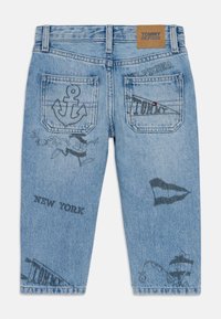 Jeans in denim azzurro con vari design ricamati, tra cui un'ancora e la scritta "NEW YORK", con un layout distintivo delle tasche posteriori.