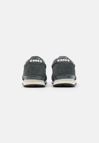 Blue suede sneakers with a black rubber sole, featuring a white logo on the heel and a sleek, minimalistic design.