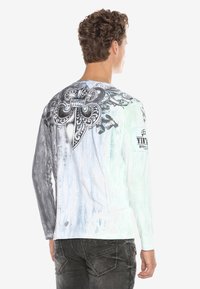 Langærmet T-shirt med et gradientdesign i grå og hvid, med et stort sort grafisk motiv på ryggen, der inkluderer detaljeret udsmykning.