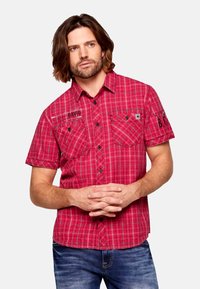 Camicia a maniche corte a quadri rossi con accenti neri, dotata di due tasche frontali e chiusure a bottoni. Il tessuto sembra leggero e traspirante.