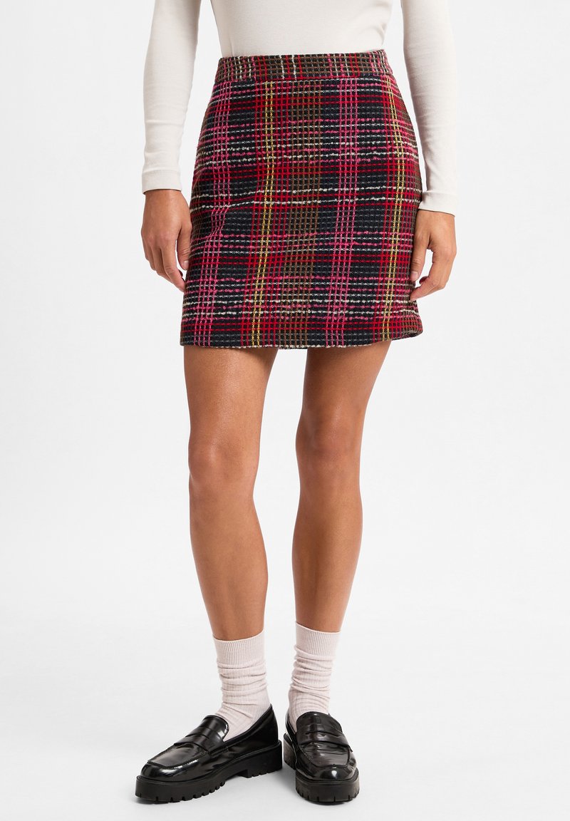 Wollen gemengde ruitjes minirok in donkere tinten met multicolor lijnen. Heeft een getailleerde taille en een rechte snit. Gepaard met zwarte instappers en sokken.