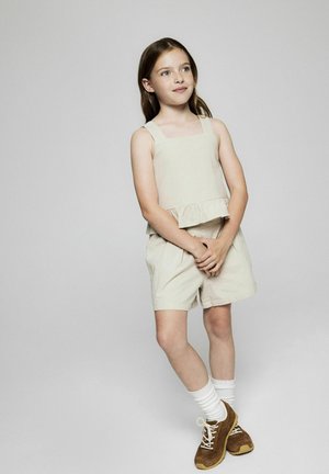 Haut en lin beige avec un ourlet volanté, associé à un short assorti. Baskets en daim marron avec des lacets blancs et des chaussettes à côtes.