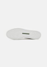 Sola di scarpa bianca in gomma testurizzata per una migliore aderenza, con un'etichetta verde che recita "NATURAL SOFT" e un design pulito e minimalista.