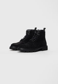 Botines de ante negro con suelas de goma, diseño de cordones y acentos de metal. Presentan una tiranta trasera y punta redonda.