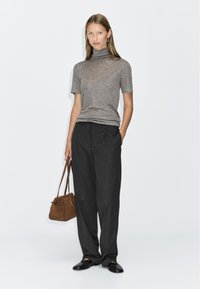 Gray turtleneck top, short sleeves, paired with dark, loose-fitting trousers. Brown suede handbag with short handles, black slip-on shoes.