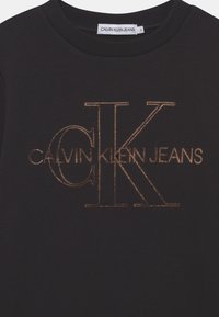 Sudadera negra con un gran logo bordado en dorado metálico, que muestra "CALVIN KLEIN JEANS" y "CK" en una fuente audaz.