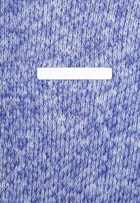 Stickat blått och vitt tyg med ett texturerat mönster. Har en vit rektangulär etikett med "ragwear" präglad i mitten.