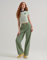 Maglietta a righe verdi e bianche con logo "Lee Crayola", abbinata a pantaloni larghi verdi con texture e sneakers gialle.