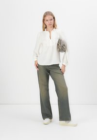 Blouse blanche à manches longues avec un col à volants, associée à un jean large vert clair et des baskets blanches. Tenant un sac à main en cuir texturé à imprimé serpent.