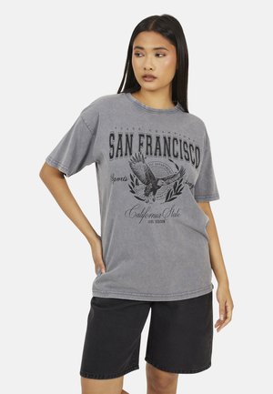 Grey oversized t-shirt with a faded finish, featuring a black graphic print of an eagle and "SAN FRANCISCO" text. Paired with black shorts.