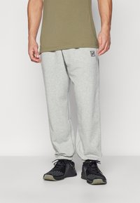 Calças de moletom cinzentas com bolsos laterais e punhos elásticos, feitas de material suave. Combinadas com sapatilhas pretas, com um padrão detalhado.