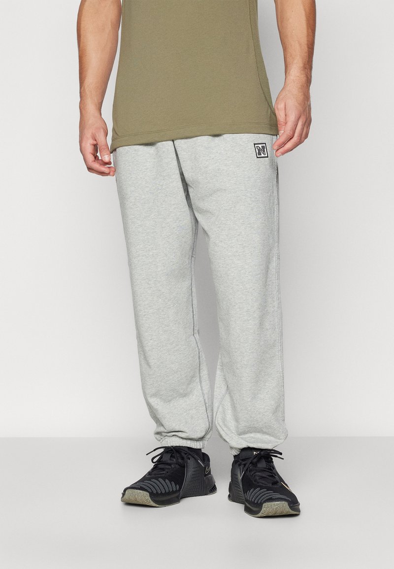 Calças de moletom cinzentas com bolsos laterais e punhos elásticos, feitas de material suave. Combinadas com sapatilhas pretas, com um padrão detalhado.