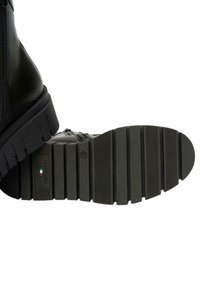 Stivale alla caviglia in pelle nera con suola in gomma spessa caratterizzata da scanalature orizzontali. Chiusura laterale con zip e dettaglio del logo sulla suola.