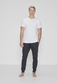 Hvid kortærmet t-shirt kombineret med mørkegrå joggerbukser. T-shirten har en rund udskæring; joggerne har elastisk linning og manchetter.