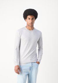 Gray long-sleeve shirt made of soft fabric, round neck, slim fit. Worn with light blue jeans, featuring a simple design and minimal detailing.