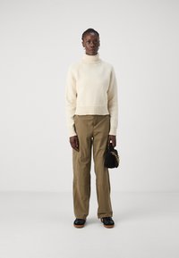 Cremefarvet turtleneck sweater med en tekstureret finish, parret med olivengrønne bukser med brede ben. Sort tekstureret håndtaske med guldkædedetalje.