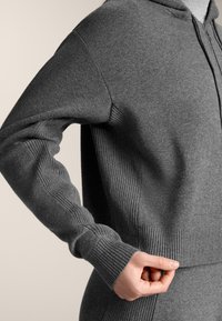 Hanorac gri cu fermoar, realizat dintr-un material moale, cu manșete și tiv striate, având o croială lejeră și detalii de design minimaliste.